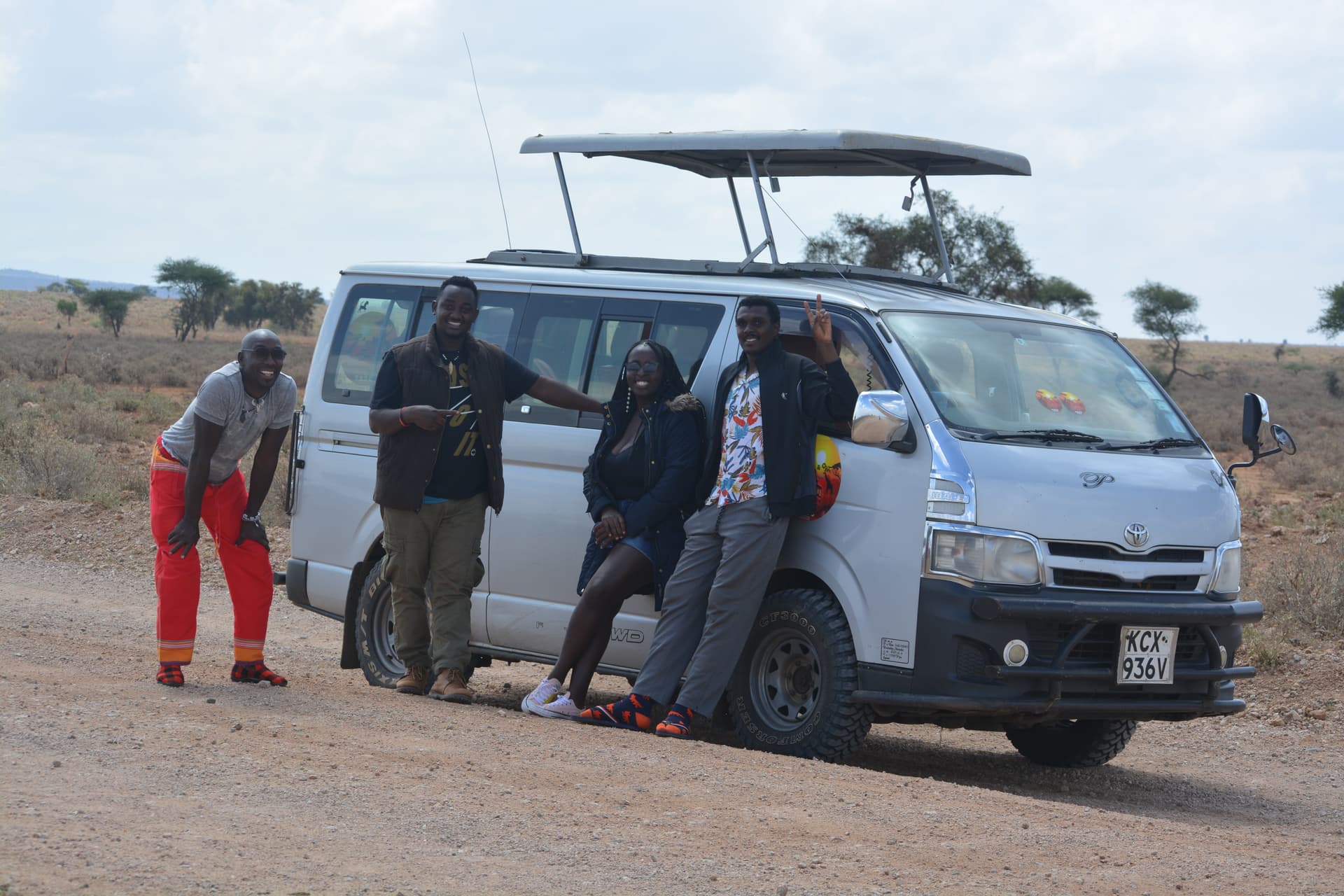 Travelers and a guide beside a pop-top safari van on a savanna track